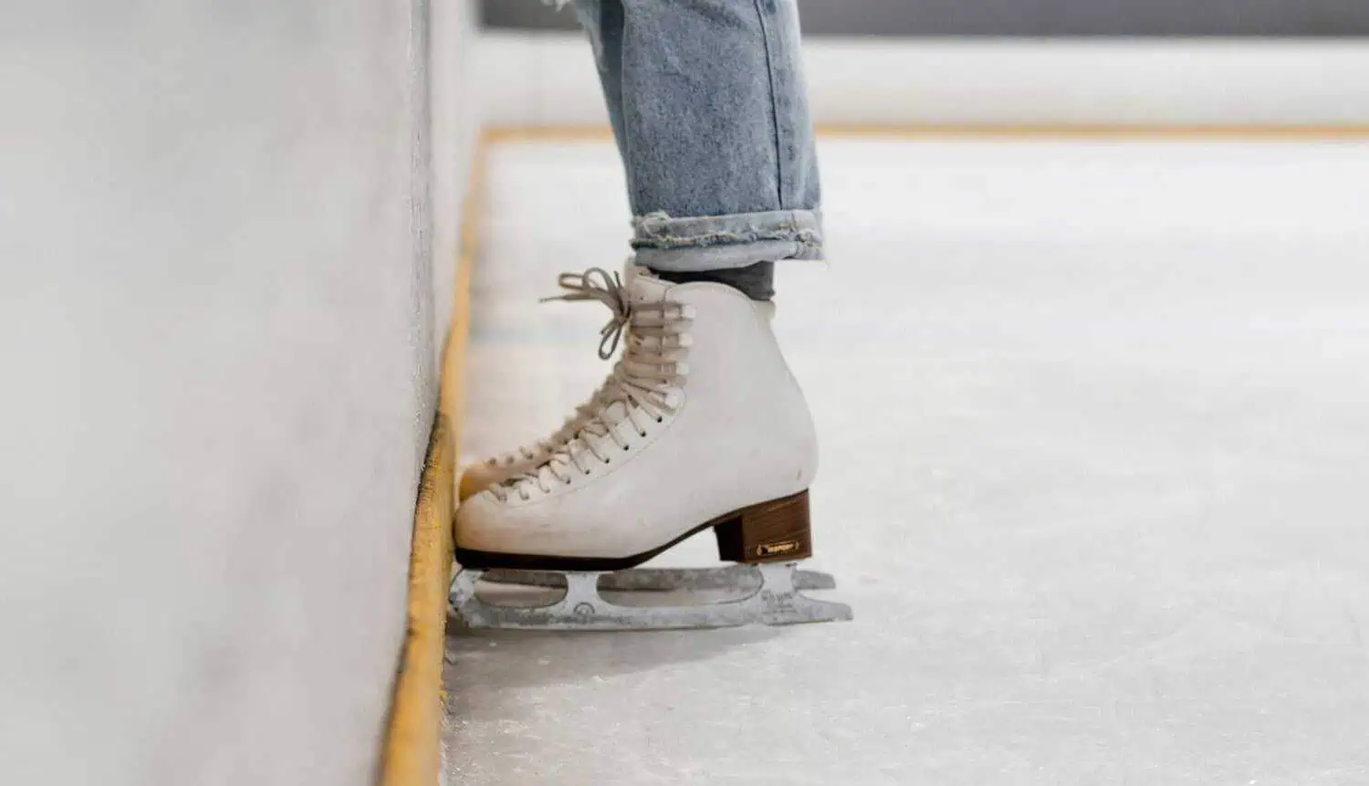 Close up of a skater's white figure skates on the ice with their toes up against the edge of the rink - how skaters get started
