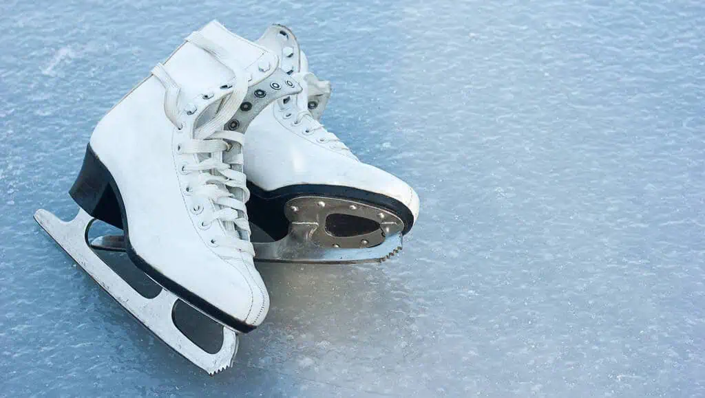 White figure skates lying on their sides, one of top of the other, on ice