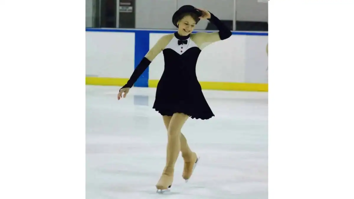 Adult figure skater wearing a tuxedo-reminiscent dress and black bowler hat in the middle of her program
