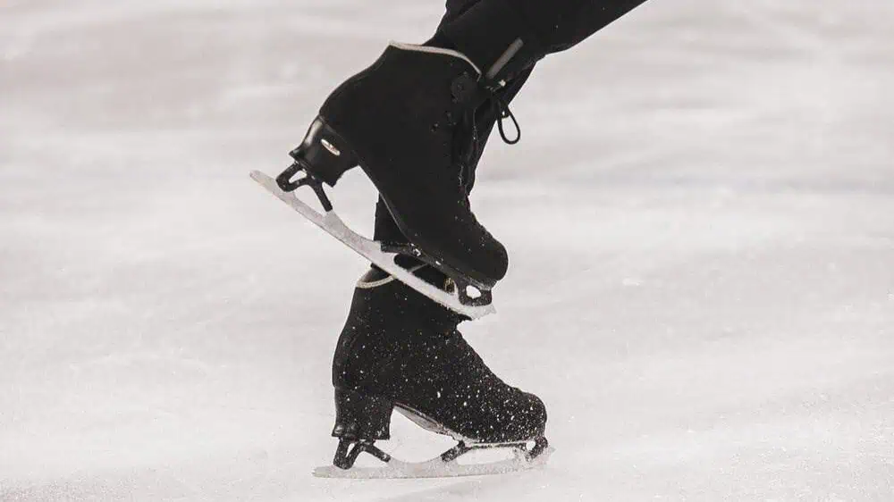 Close up of men's black figure skates on ice mid step