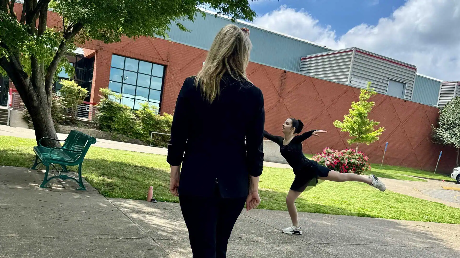 Figure skater in landing position outside the skating rink doing her off-ice warmup as her coach watches