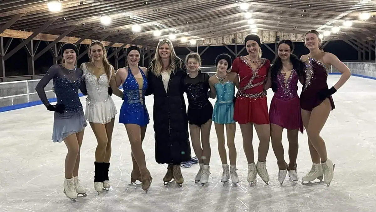 Eight teenage girls wearing a variety of figure skating dresses