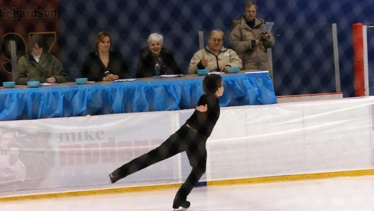 Panel of judges sitting rink-side watching a boy perform his program