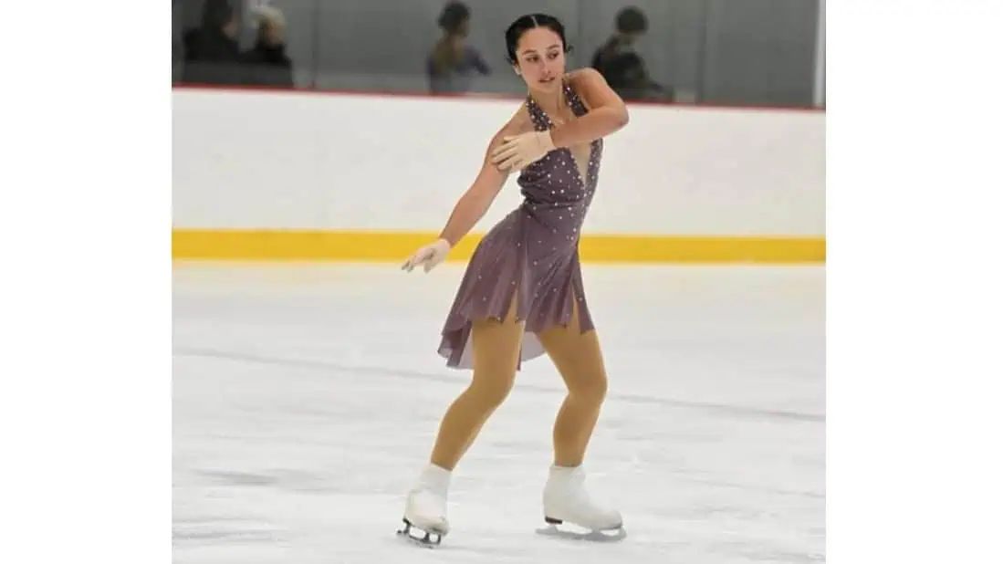 Female figure skater in a brown ice dance dress in the opening pose of her program