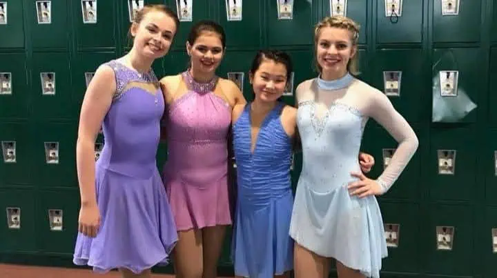 Four teenaged female figure skaters wearing skating dresses appropriate for testing - fairly simple styles in varying shades of blue and lavender